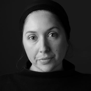 Black and white portrait of a woman wearing a dark top and headband, looking at camera.
